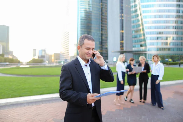 Businessperson talking by smartphone with employees in backgroun