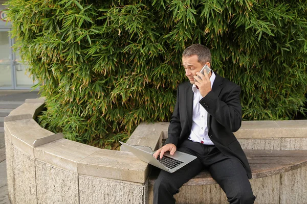 Gerente conversando por smartphone e trabalhando com laptop fora em — Fotografia de Stock
