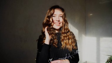 Genç kadın kıvırcık saçlı kameraya bakarak gülümseyen,