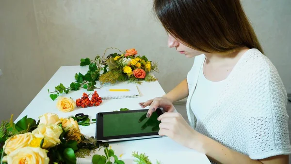 Encantadora florista chica mira las tendencias de la tableta de la temporada cuando co — Foto de Stock