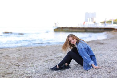 Gülümseyen genç kadın kumsalda aittir ve kamera, oturan pozlar 