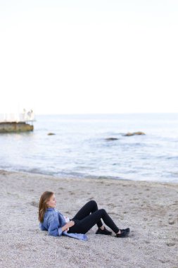 Gülümseyen genç kadın kumsalda aittir ve kamera, oturan pozlar 