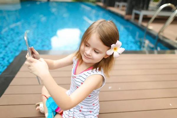 Pequeña linda chica utiliza la tableta en la piscina de fondo, wearin — Foto de Stock