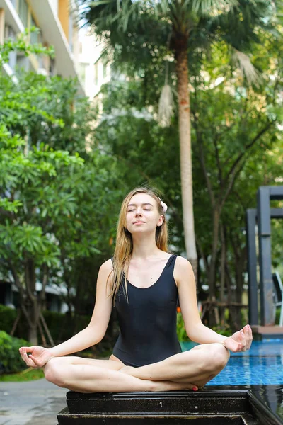 Mujer sana sentada en posición de loto, haciendo yoga junto a la piscina — Foto de Stock