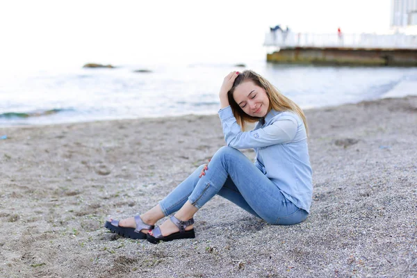 Χαμογελαστά νεαρή γυναίκα στηρίζεται στην παραλία και θέτει στην κάμερα, κάθεται — Φωτογραφία Αρχείου