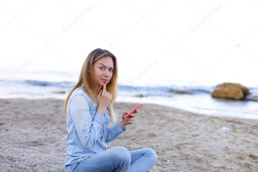 Lovely girl chatters on telephone with smile and sits on beach n