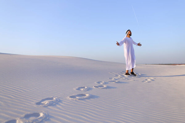 Joyful male Muslim walks through white sand desert and enjoys li