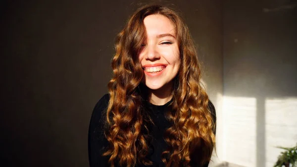 Młoda kobieta uśmiechnięty, patrząc na kamery z kręconymi włosami — Zdjęcie stockowe