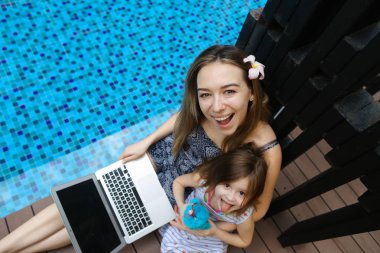Yakın çekim kadın anne, kızı ve Yüzme Havuzu arka plan üstünde laptop