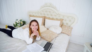 Güzel kız Freelancer kullanır Laptop için iş, bırakır yatak odasında büyük yatakta ve