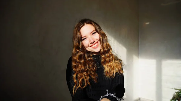 Młoda kobieta uśmiechnięty, patrząc na kamery z kręconymi włosami — Zdjęcie stockowe