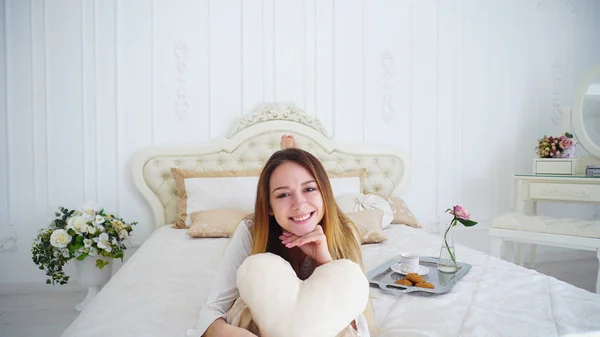 Retrato de linda hembra sosteniendo almohada-corazón, posando y sonriendo mientras miente — Foto de Stock