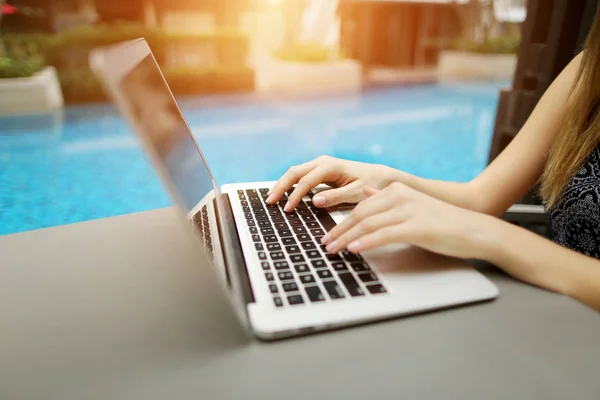 Cerrar las manos de la mujer presionando el teclado en el ordenador portátil día soleado piscina — Foto de Stock