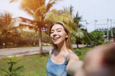 neşeli kadın objektif kamera, holding selfie alarak avuç içi ve yeşil çim ile güneşli Tayland seyahat
