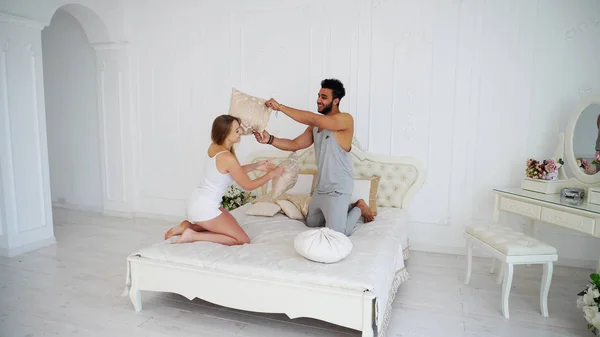 Casal feliz se comporta como crianças pulando na cama em Bedro brilhante — Fotografia de Stock