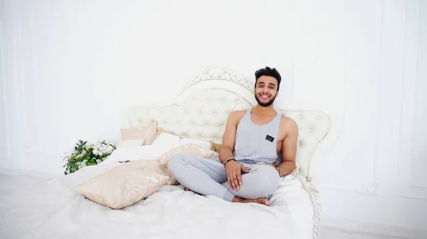 Молода арабська людина розслабляється і посміхається лежачи на ліжку в яскравому Б — стокове фото
