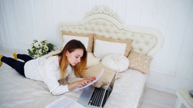 Güzel kız Freelancer kullanır Laptop için iş, bırakır yatak odasında büyük yatakta ve