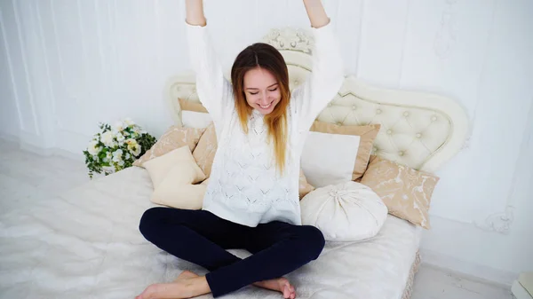 Chica atractiva disfruta bailando y sentado en la cama, sonriendo en los dormitorios brillantes . — Foto de Stock