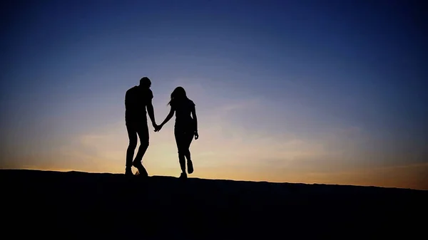 Жінка і чоловік, тримаючись за руки, піднімаються на вершину піщаного пагорба — стокове фото