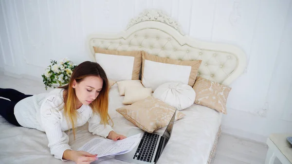 Mooi meisje Freelancer gebruikt Laptop voor werk, legt op het grote Bed in de slaapkamer en — Stockfoto