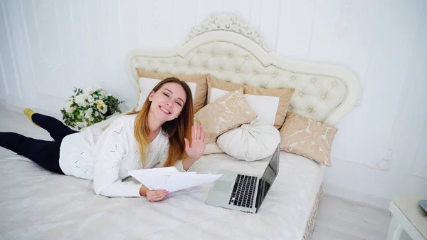 Mooi meisje Freelancer gebruikt Laptop voor werk, legt op het grote Bed in de slaapkamer en — Stockfoto