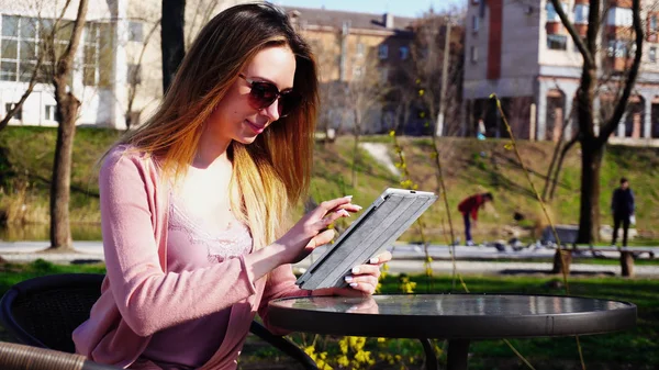 Chica encantadora trabajando con la tableta en el parque y descansando en el sol gla — Foto de Stock