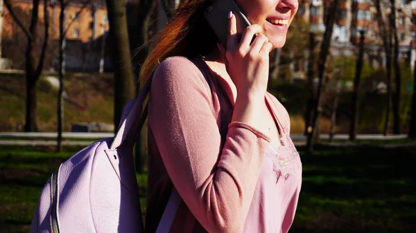 Estudiante alegre caminando en el parque y hablando por teléfono inteligente . — Foto de Stock