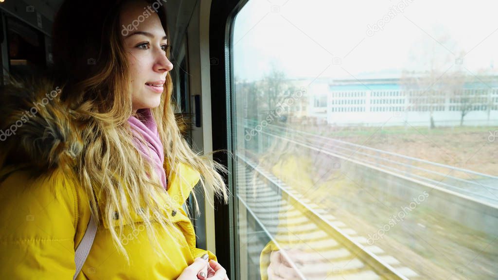 Lovely young woman riding in train and looking at  landscape out