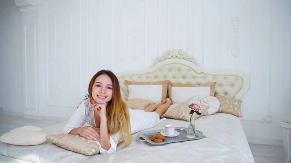 Meisje Model glimlachend op Camera liggend op Bed in lichte slaapkamer. — Stockfoto