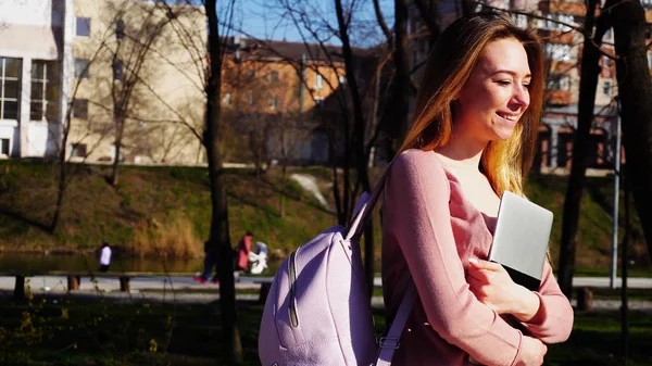 Joyeux étudiant marchant dans le parc avec ordinateur portable et sac à dos  . — Photo