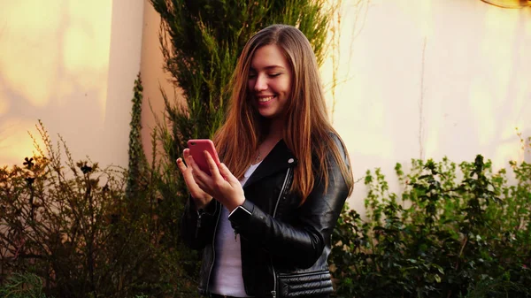 Piękna dziewczyna pisania wiadomości przez smartfon w przypadku różowy w pobliżu gr — Zdjęcie stockowe