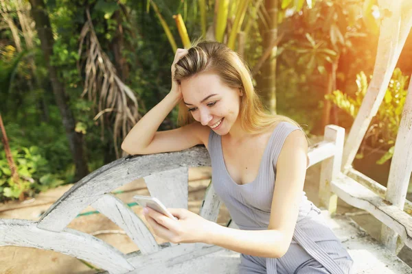 Woman uses smart phone on sunny day, background of sunshine green palms in Thailand, Phuket