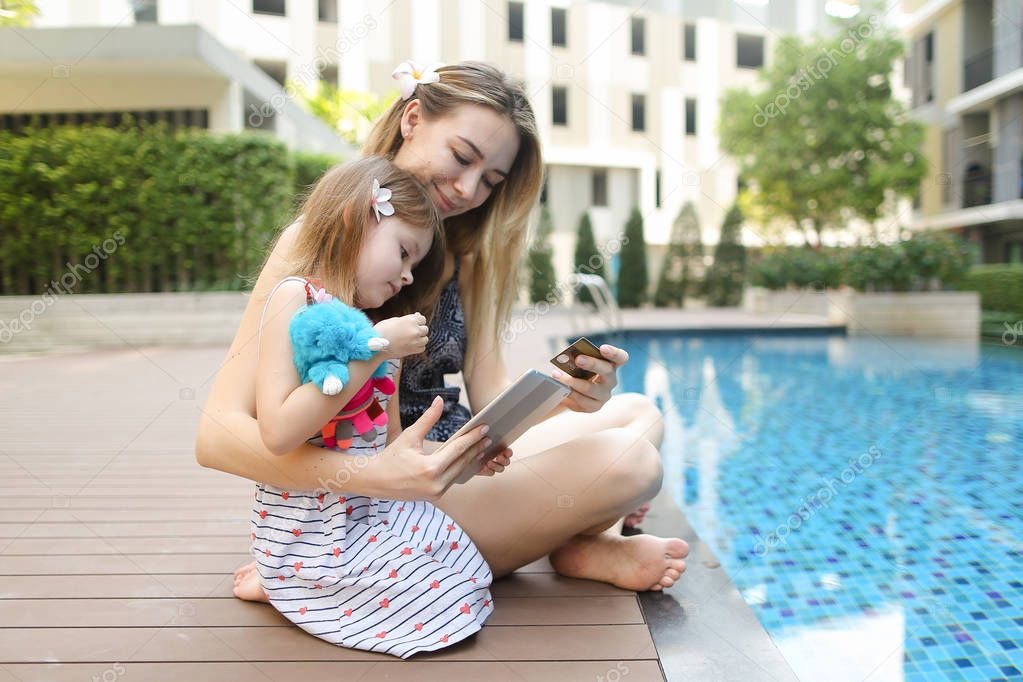 Young mother working on vacations with laptop near swimming pool