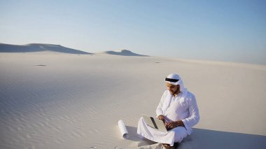 Kum üstünde laptop ile oturan Müslüman Arap BAE Şeyh mimar 