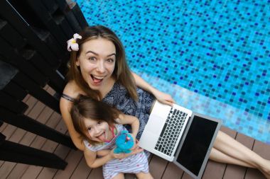 Yakın çekim kadın anne, kızı ve Yüzme Havuzu arka plan üstünde laptop
