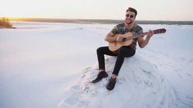 Arap yakışıklı arasında kum tepe üzerinde duran gitar çalmak