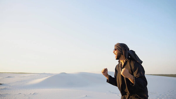 Happy fellow Arabian, walks through desert, smiles and enjoys li