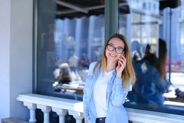 Mujer hablando por teléfono inteligente cerca de la ventana de la cafetería . — Foto de Stock