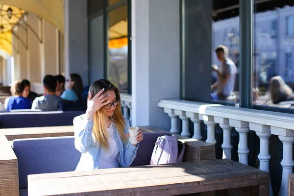 Chica joven sentada en la cafetería de la calle y beber café . — Foto de Stock