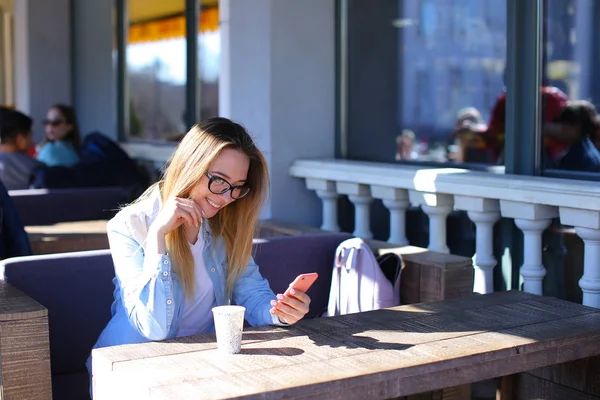 Dziewczyna za pomocą smartfona i siedzi w kawiarni, z filiżanką herbaty. — Zdjęcie stockowe