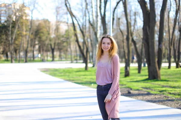 Bella ragazza guardando la fotocamera, sorridente e passeggiando nel parco primaverile . — Foto Stock