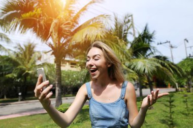 neşeli kadın konuşmak ile akıllı telefon, avuç içi ve yeşil çim ile güneşli Tayland seyahat