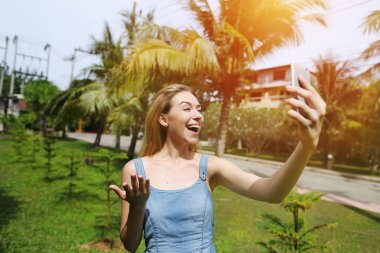 neşeli kadın yapma video ara ile akıllı telefon, avuç içi ve yeşil çim ile güneşli Tayland seyahat