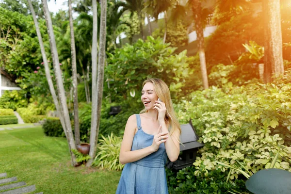 sunshine young woman talking call with phone and smiling on palms and house background