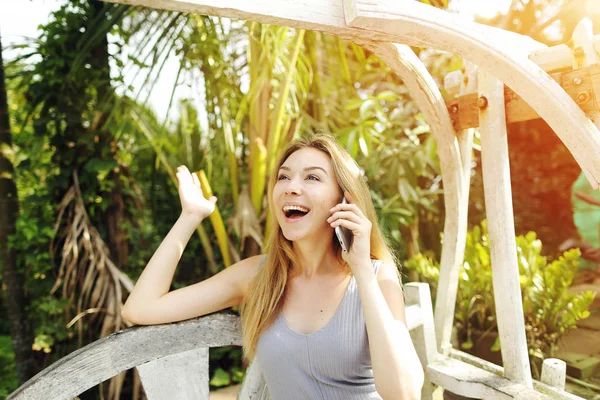 Mulher loira tem ótimas notícias, falando no smartphone para o trabalho no dia ensolarado, fundo de sol palmas verdes na Tailândia, Phuket viagem — Fotografia de Stock