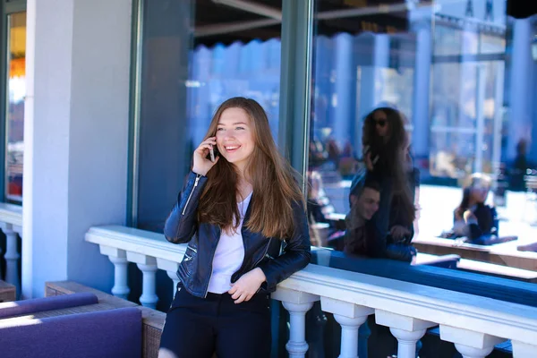 Young female person talking by smartphone near window of street cafe.