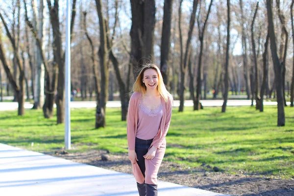 Sorridente bella ragazza guardando la fotocamera e passeggiando nel parco primaverile . — Foto Stock