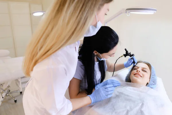 Young lady at cosmetology cabinet getting permanent makeup procedure by cosmetologist.