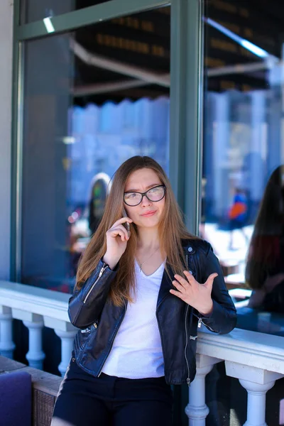 Щаслива жінка в окулярах і розмовляє по смартфонах у вуличному кафе . — стокове фото