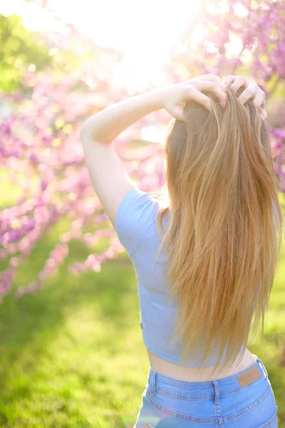 Blond kvinna som står i solen strålar med grönt gräs och blossom bakgrund. — Stockfoto